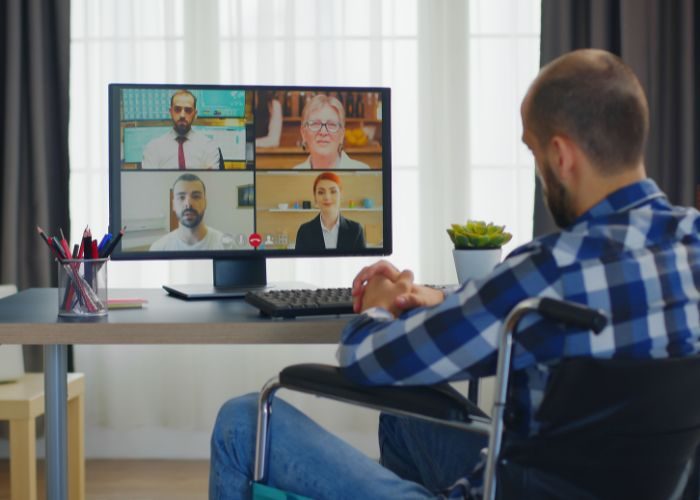 Mand i kørestol holder online-møde. På skærmen ses ansigterne af fire andre mødedeltagere.