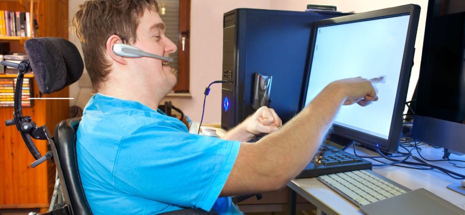 Mand i elektrisk kørestol sidder ved stationær computer og arbejder.